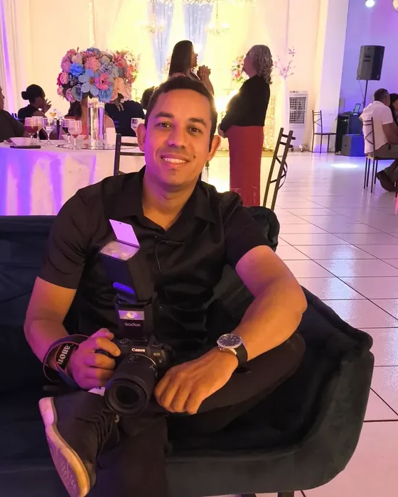 Greidson sorrindo com a câmera nas mãos durante uma festa