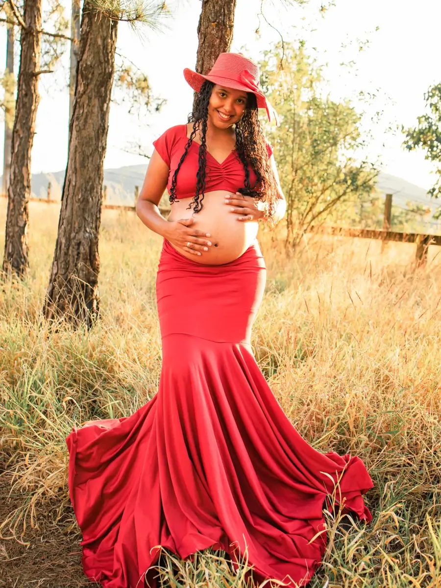 Gestante de vestido vermelho e chapéu no campo